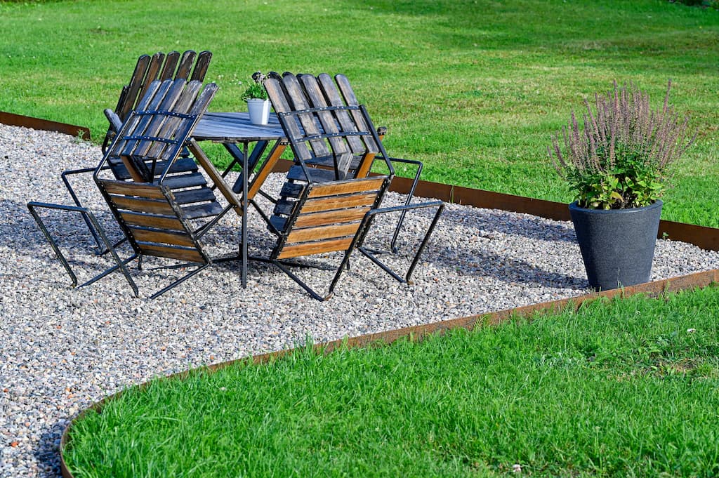 corten steel garden edging with grass on one side and stones on the other with a table and chairs and plant pot in the background