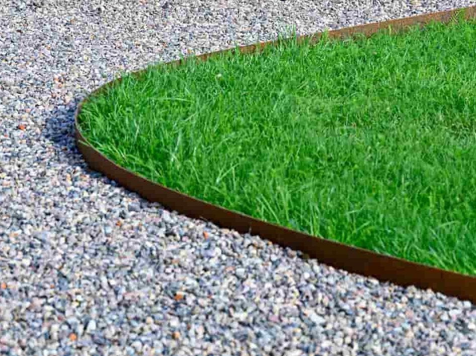 a curved piece of corten steel edging with green grass on the right and stones on the left